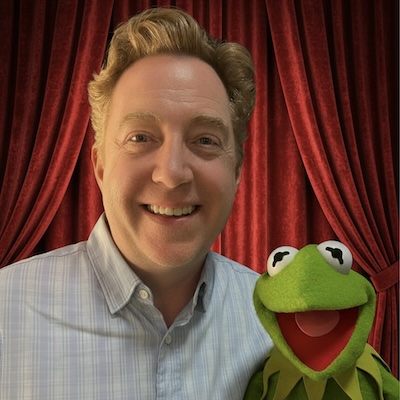 Kelly Younger standing with kermit in front of red curtain
